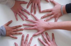 Mehrere Hände liegen flach auf weißer Oberfläche und bilden einen lockeren Kreis.