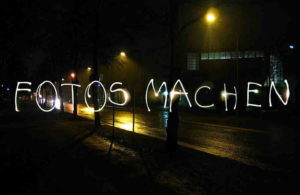 Bei Nacht entstandener Schriftzug Fotos Machen durch Lichtmalerei auf nasser Straße mit Laternen.