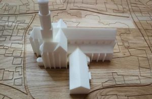 Weißes 3D-Gebäudemodell auf einer Holzplatte mit eingravierten Baugrundrissen