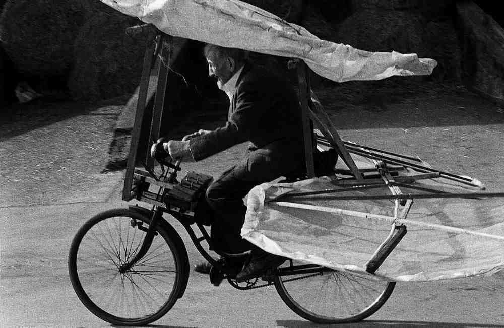 Mann fährt Fahrrad mit befestigten Flügeln und Fluggerät-ähnlicher Struktur.