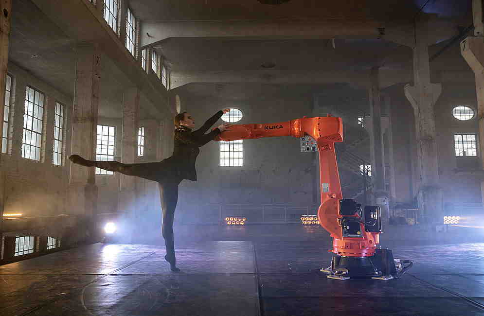 Tänzerin in Aktion mit dem Arm eines Industrie-Roboters