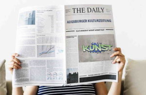 Person liest Zeitung THE DAILY mit Titel AUGSBURGER KULTURZEITUNG und Graffiti-Bild KÜNST.