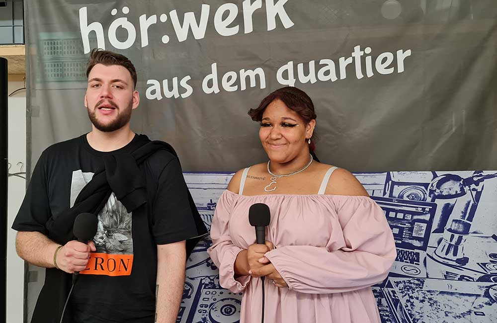 werk aus dem quartier und halten jeweils ein Mikrofon.