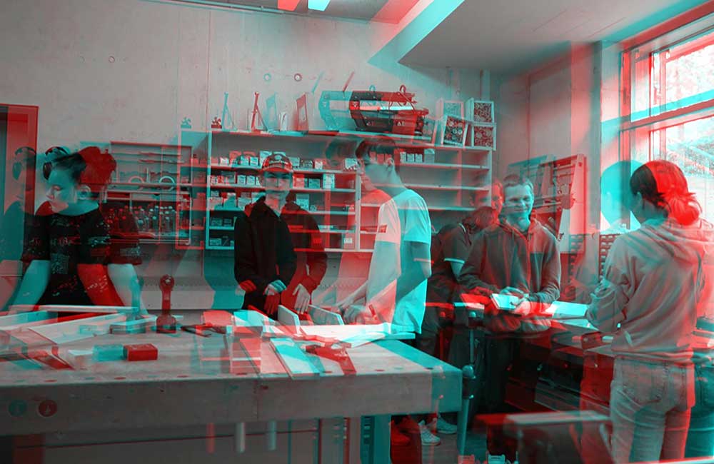 Jugendliche arbeiten gemeinsam in einer Werkstatt mit Holz und Werkzeugen vor Regalen.