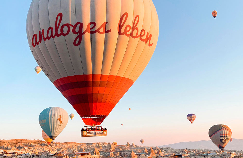Mehrere Heißluftballons schweben über felsiger Landschaft bei klarem Himmel im Sonnenlicht.